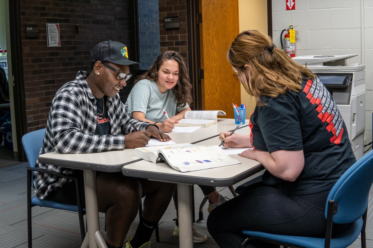 3 people sitting at a table doing homework together